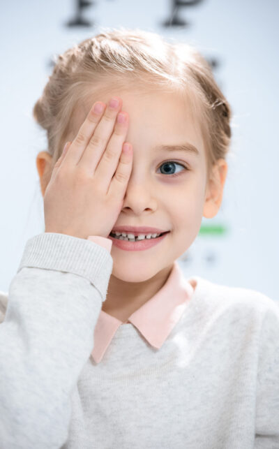 smiling little kid closing eye with eye chart behind